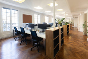 Grand open-space lumineux réalisés entièrement avec du mobilier de réemploi : écrans d'ordinateurs, bureaux, chaises, étagères et plantes.